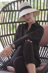 Woman wearing a black lace long-sleeve shirt and wide-brimmed hat, sitting comfortably in a stylish wicker chair.